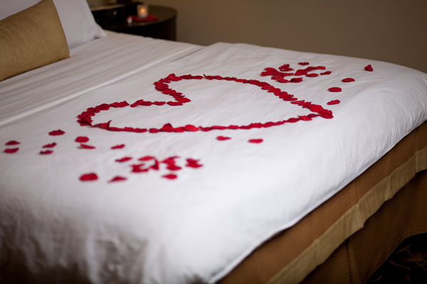 Red rose flower petals in the shape of a heart on top of a bed.